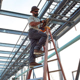 Man on ladder wearing Ariat Rebar M4 DuraStretch pants, using a power tool on a construction site.