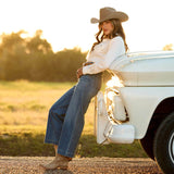 Woman wearing Ariat Perfect Rise Jazmine Wide Leg Crop Jeans and cowboy hat leaning against a vintage truck at sunset.