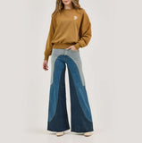 Woman wearing a brown Wrangler sweatshirt with unique denim flared pants, showcasing a trendy style.
