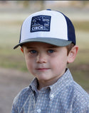 Cinch Boys Youth Trucker Cap in navy and olive worn by a young boy, featuring a classic design and bucking horse graphic.