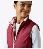 Ariat Youth Bella Reversible Insulated Vest in maroon, worn by a smiling girl with floral lining, ready for outdoor adventures.