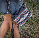 Woman wearing a Guadalupe Serape Lily Crossbody bag while standing in grass, showcasing its rustic design. Serape crossbody bag.