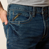 A close-up of a man's hand in the pocket of Rebar M4 work jeans showcasing the Ariat branding and durable denim fabric.