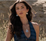 Woman wearing a Flower Rowel Necklace and floral earrings in a serene natural setting.