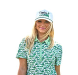 Hooey hat worn by a smiling woman in a green polo, featuring a golf course landscape design.