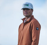 Hooey hat featuring golf course landscape design worn by a man in a stylish beige pullover.