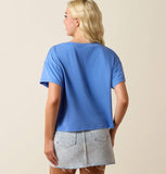 Back view of a woman wearing an Ariat Women's Cowboy Club Cropped Graphic T-Shirt in blue with a grey skirt.