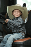 Cinch toddler wearing a paisley long sleeve western shirt and cowboy hat, ready for the rodeo.