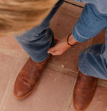 Close-up of a person wearing Tecovas The Earl Men's Roper Boot in Scotch Goat while adjusting denim jeans.