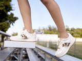 Ariat Ranch Runner Trainer in Bright Cream & Gilded Leopard Hair-On worn by a person on bleachers.